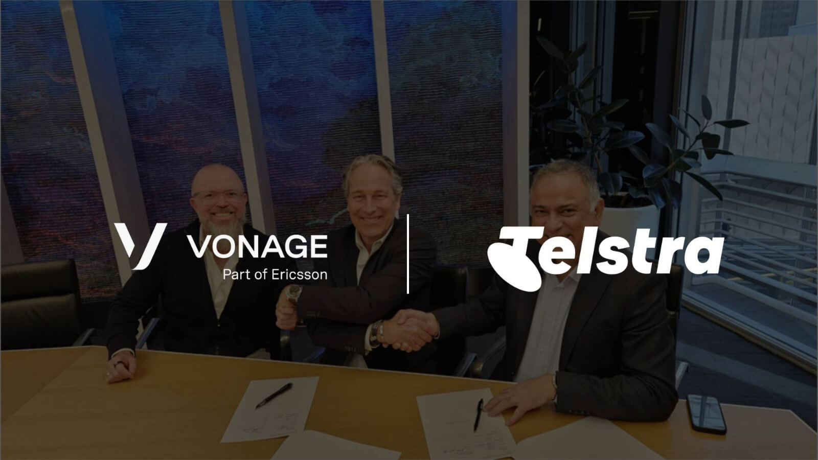 Executives seated at a table signing papers for Telstra and Vonage.