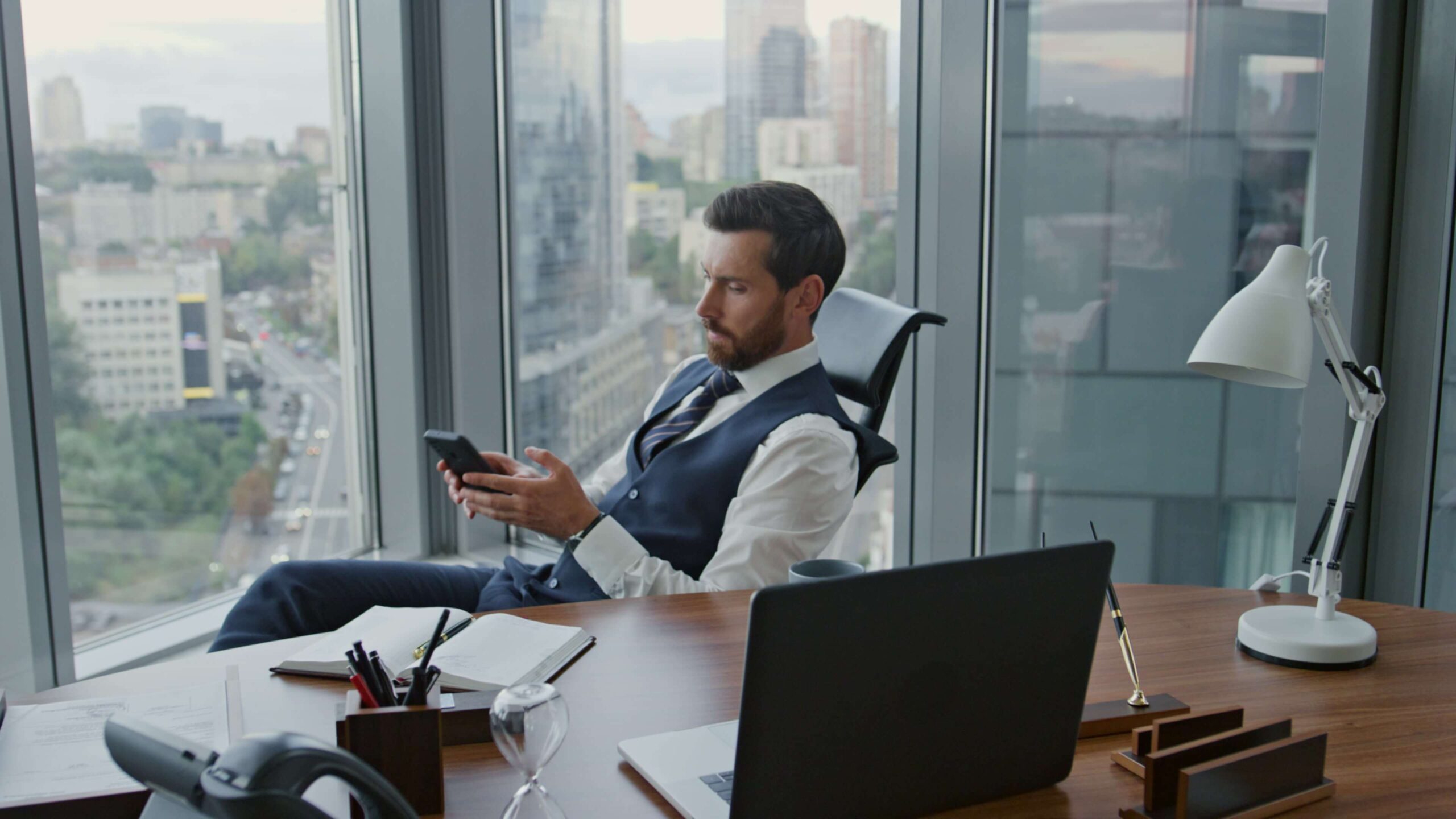 Businessman-reading-phone-message-sitting-in-office-with-other-devices