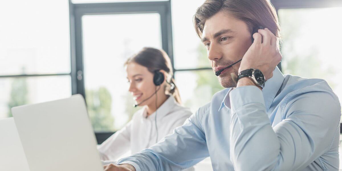 A man and woman are seated in a call center, concentrating on their laptops as they handle customer inquiries